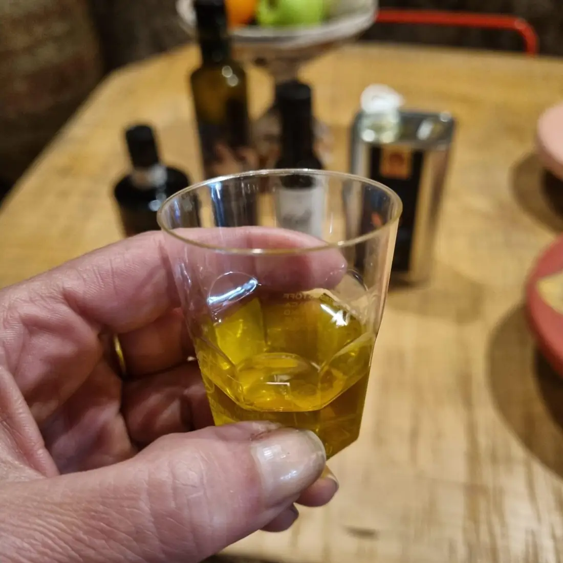 Un bicchierino di olio extravergine del Lazio in mano, con le bottiglie sul tavolo