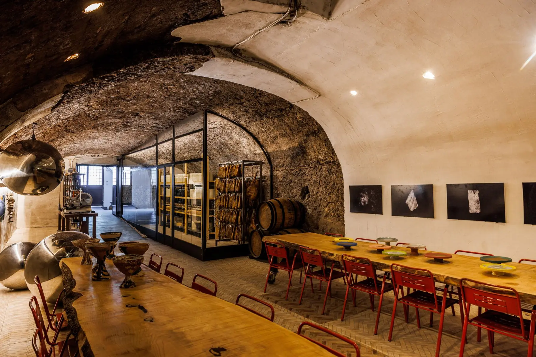 I due tavoli lunghi nella grotta, con le forme e i salumi dietro il vetro
