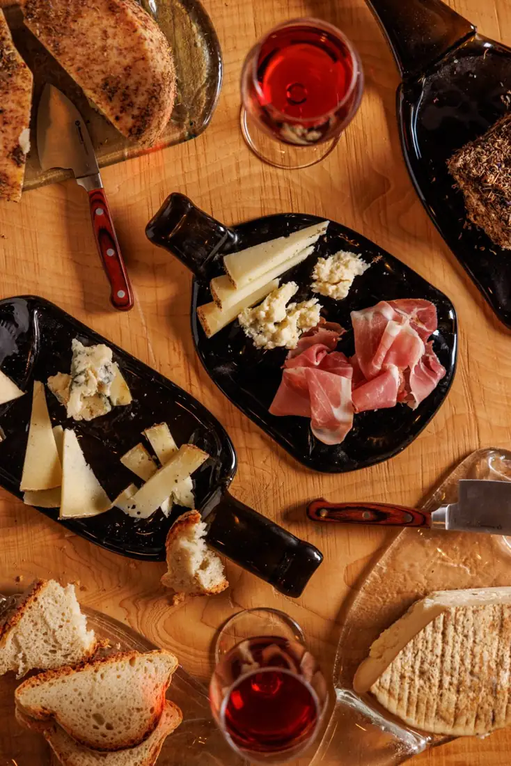 I taglieri con i formaggi affinati in grotta, il prosciutto, il pane e due calici di vino, visti dall'alto
